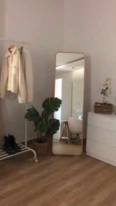 a white room with a mirror, coat rack and shoes on the floor in front of it