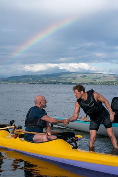 two men are shaking hands on a kayak with a rainbow in the background