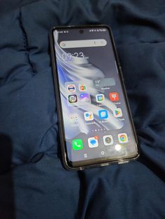 an open cell phone laying on top of a blue bed sheet covered in black sheets