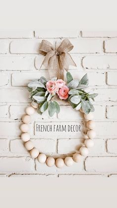 a white brick wall with a wreath and flowers on it that says french farm decor