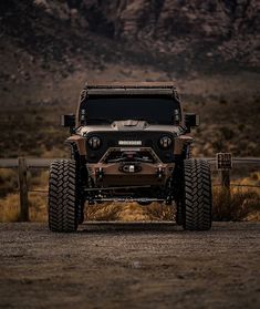 a jeep parked in front of a fence on a dirt road with mountains in the background