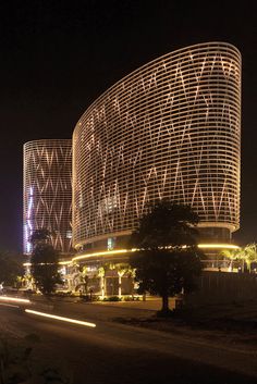 two circular buildings lit up at night with lights on the side and trees in front