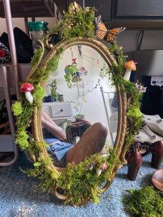 a mirror that is sitting on the ground with moss growing around it and a person's reflection in the mirror