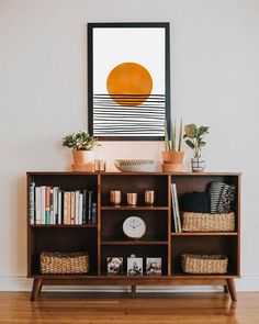 a shelf with books and plants on it in front of a wall mounted art piece