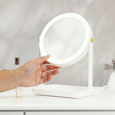 a woman's hand is holding an illuminated ring light in front of a mirror