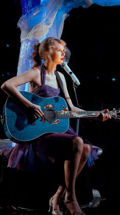 a woman in a purple dress holding a blue guitar and singing into a microphone on stage