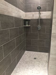 a walk in shower sitting next to a tiled wall with shelves on each side and a hand held shower head