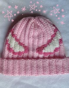 a pink knitted hat sitting on top of a white sheet with stars in the background