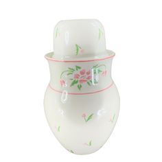 a white vase with pink and green flowers on the bottom, sitting in front of a white background