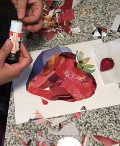 someone is making a heart shaped paper collage with strawberries on the table next to it