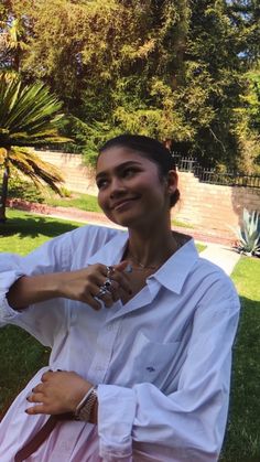 a woman sitting in the grass with her hands on her hips and smiling at the camera