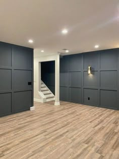 an empty room with wood flooring and black painted walls, along with stairs leading up to the second floor