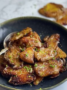 a black bowl filled with fried meat and garnished with green onions on the side