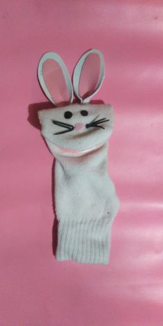 a white knitted bunny hat with ears hanging from it's side on a pink background