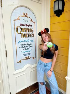 a woman standing in front of a sign holding a frisbee and pointing at the camera