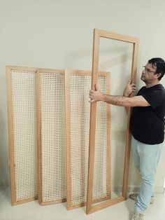 a man standing next to a tall wooden screen with holes in the side and one hand on it