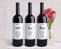 three bottles of wine sitting next to a vase with flowers in it on a table