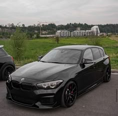 two cars parked side by side in a parking lot with grass and buildings in the background