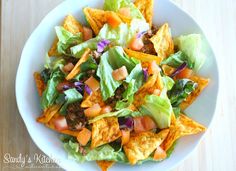 a white bowl filled with lettuce and tortilla chips on top of a wooden table