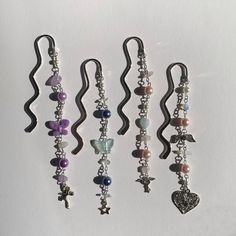 five different necklaces hanging from hooks on a white wall, one with charms and the other with beads