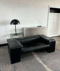 a black leather couch sitting on top of a cement floor next to a white wall