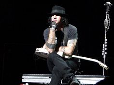 a man sitting on top of a bench holding a guitar in his right hand and wearing a hat