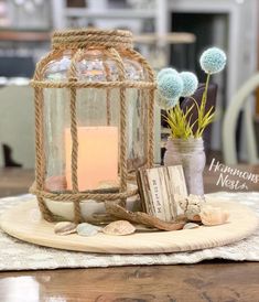 a candle is sitting in a glass lantern on a plate with seashells and driftwood