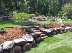 a stone wall in the middle of a yard with grass and rocks around it, surrounded by trees