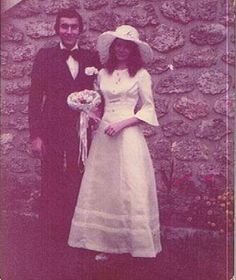 an old photo of a man and woman standing next to each other in front of a stone wall