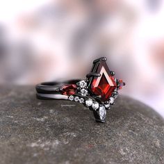 a red and black diamond ring sitting on top of a rock with other rings around it