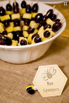 fruit skewers in a bowl on a table next to a honeybee stick