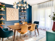 a dining room with blue walls and wooden table surrounded by chairs in front of a window