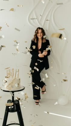 a woman standing in front of a cake with gold confetti falling from it