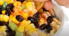 a person is scooping corn into a bowl with black olives and green peppers