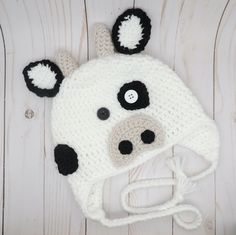 a crocheted cow hat with black and white ears is laying on a wooden surface