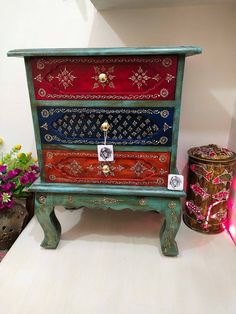 an old chest with many different colors and designs on the front, sitting next to a potted plant