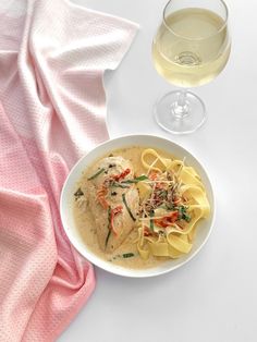 a white bowl filled with pasta and sauce next to a glass of wine on top of a pink towel