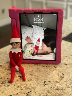 an elf is laying in bed next to a photo frame with the image of a baby on it