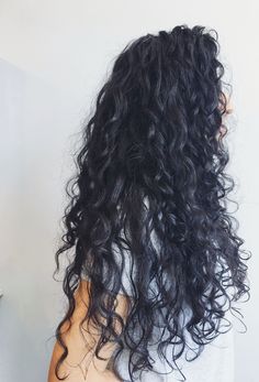 the back of a woman's head with long, curly hair in front of a white wall