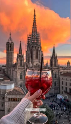 a person holding up a wine glass in front of a cityscape at sunset