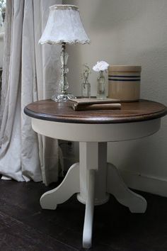 a white table with a lamp and some flowers on it next to a curtained window