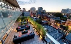 an outdoor deck with couches, tables and plants on it in the city at night