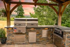 an outdoor kitchen with stainless steel appliances and grilling area under a pergolated roof