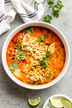 a white bowl filled with soup and garnished with cilantro, limes, and tortilla chips