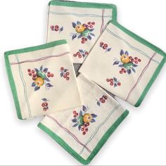 four embroidered napkins with flowers and berries on them, all in green trimming