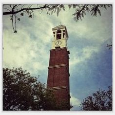 a tall brick clock tower with a white clock on it's side and trees in the foreground