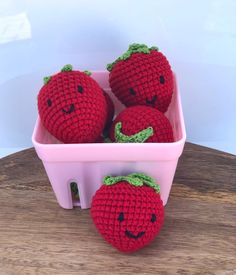 four crocheted strawberries in a pink container with faces drawn on the sides