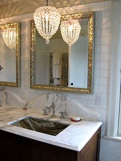 a bathroom with marble counter tops and gold framed mirrors above the sink, along with two chandeliers