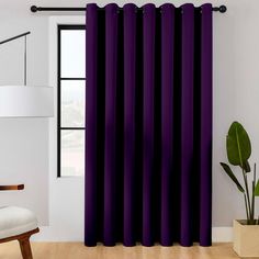 a living room with purple curtains and a white chair in front of the window that has a potted plant next to it