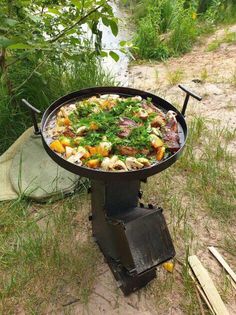 an outdoor bbq grill with meat and vegetables cooking on it in the grass next to a river